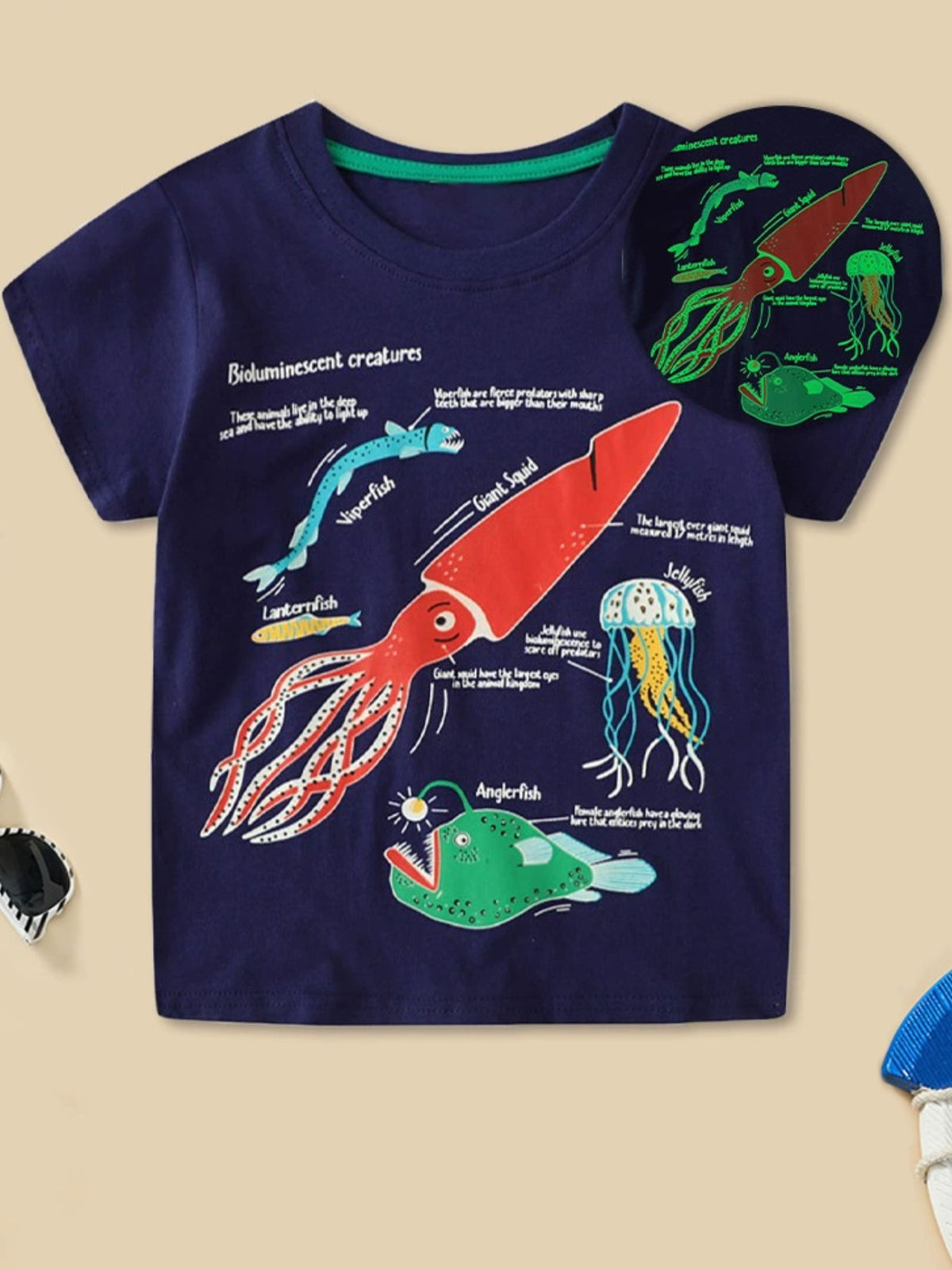 Dark navy children's t-shirt with colorful bioluminescent sea creatures print and glowing inset, front view