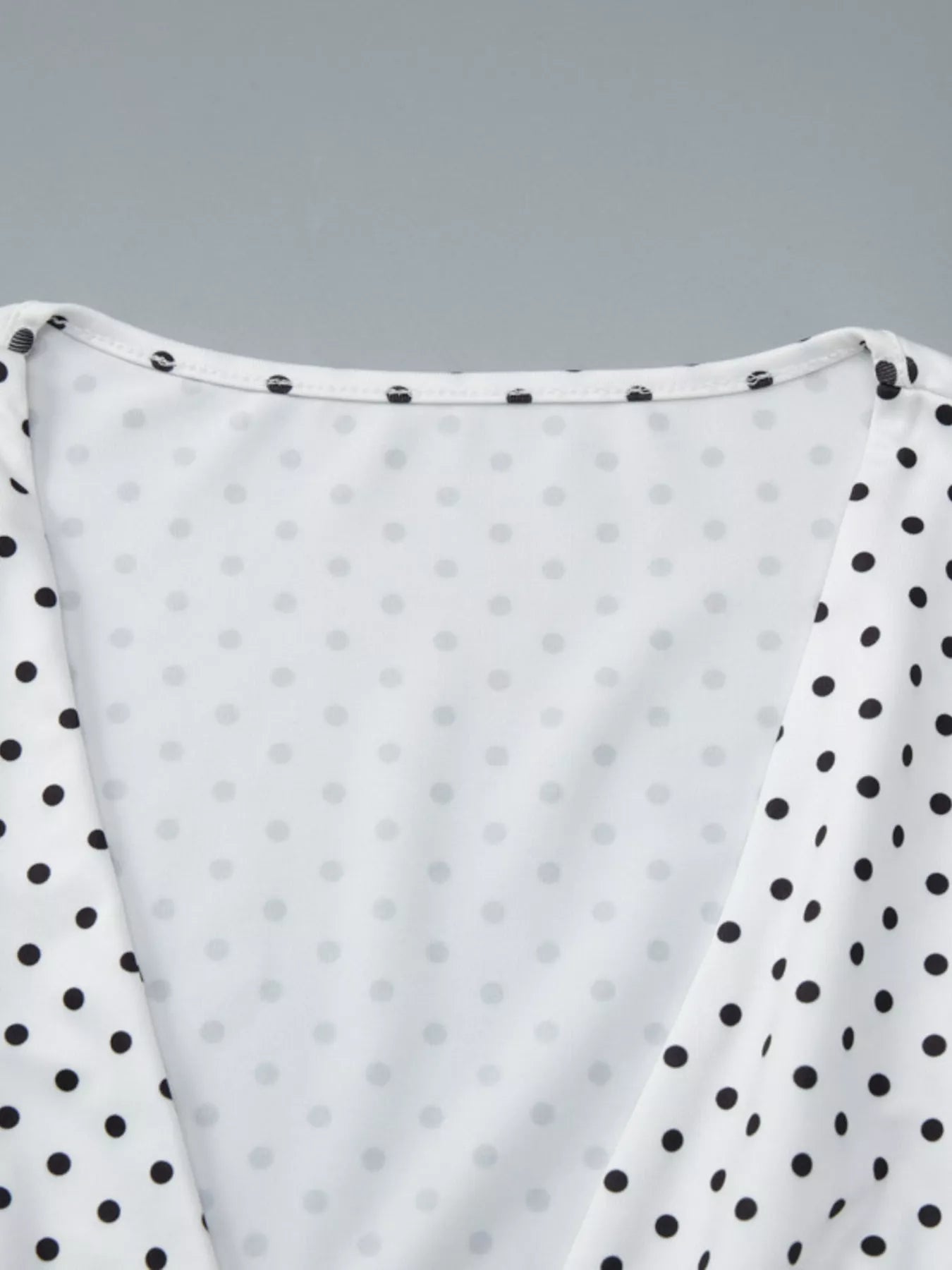 Close-up detail of the white polka dot top showing the ruched V-neckline and contrasting black dotted sleeves