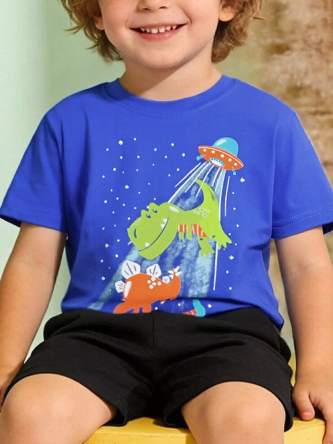 Children's royal blue short-sleeve T-shirt featuring a dinosaur and UFO graphic.