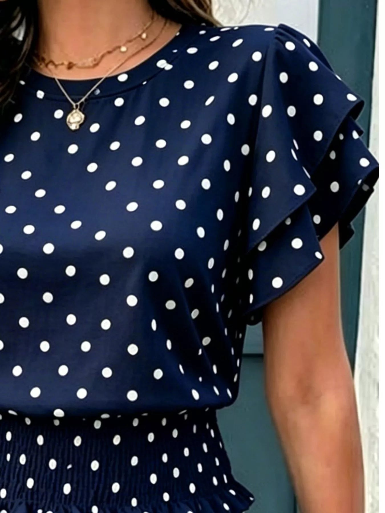 Navy polka dot blouse with layered ruffle sleeves and smocked waist detail, shown on a model