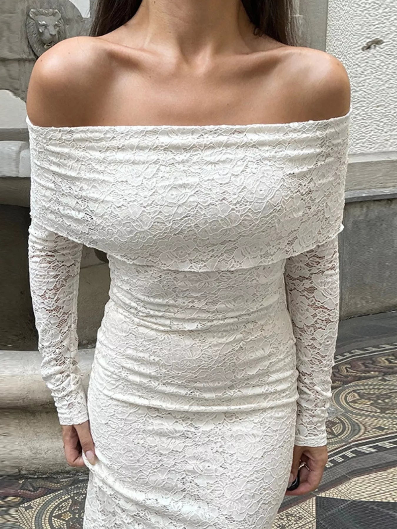 Close up view of a white off shoulder lace dress bodice showing the floral lace pattern