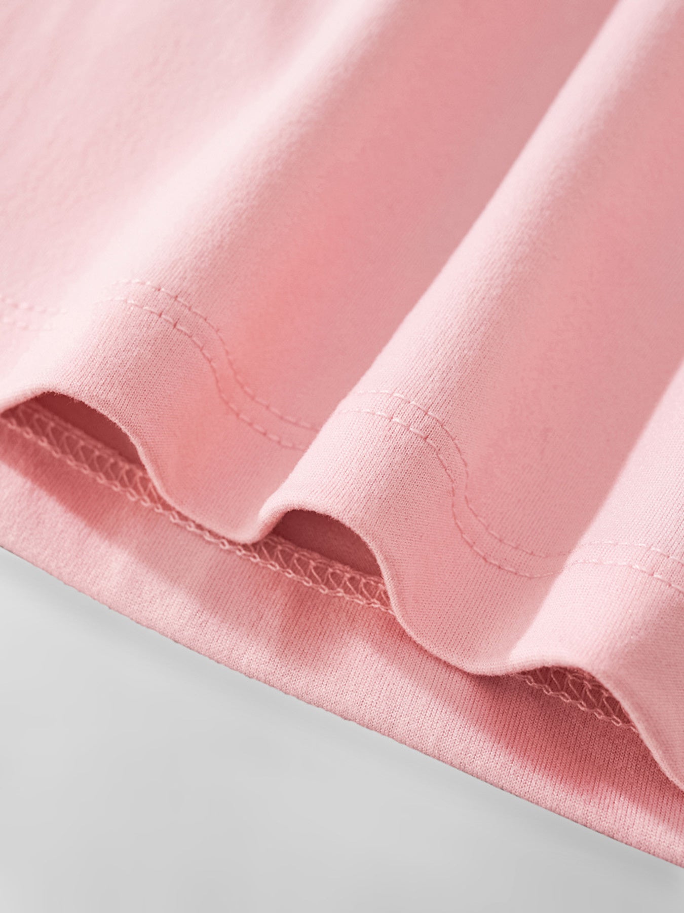 Close-up of dusty pink children's tee hem stitching and soft fabric fold