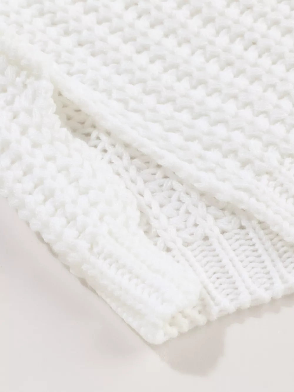 Close view of white chunky knit fabric and ribbed hem of a slouchy sweater.