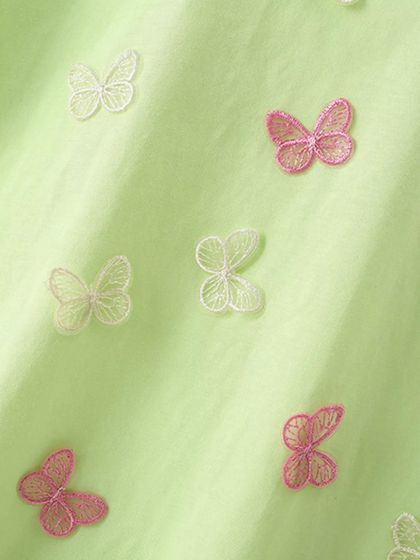 Close view of pink and white butterfly appliques scattered across the light green children's tee