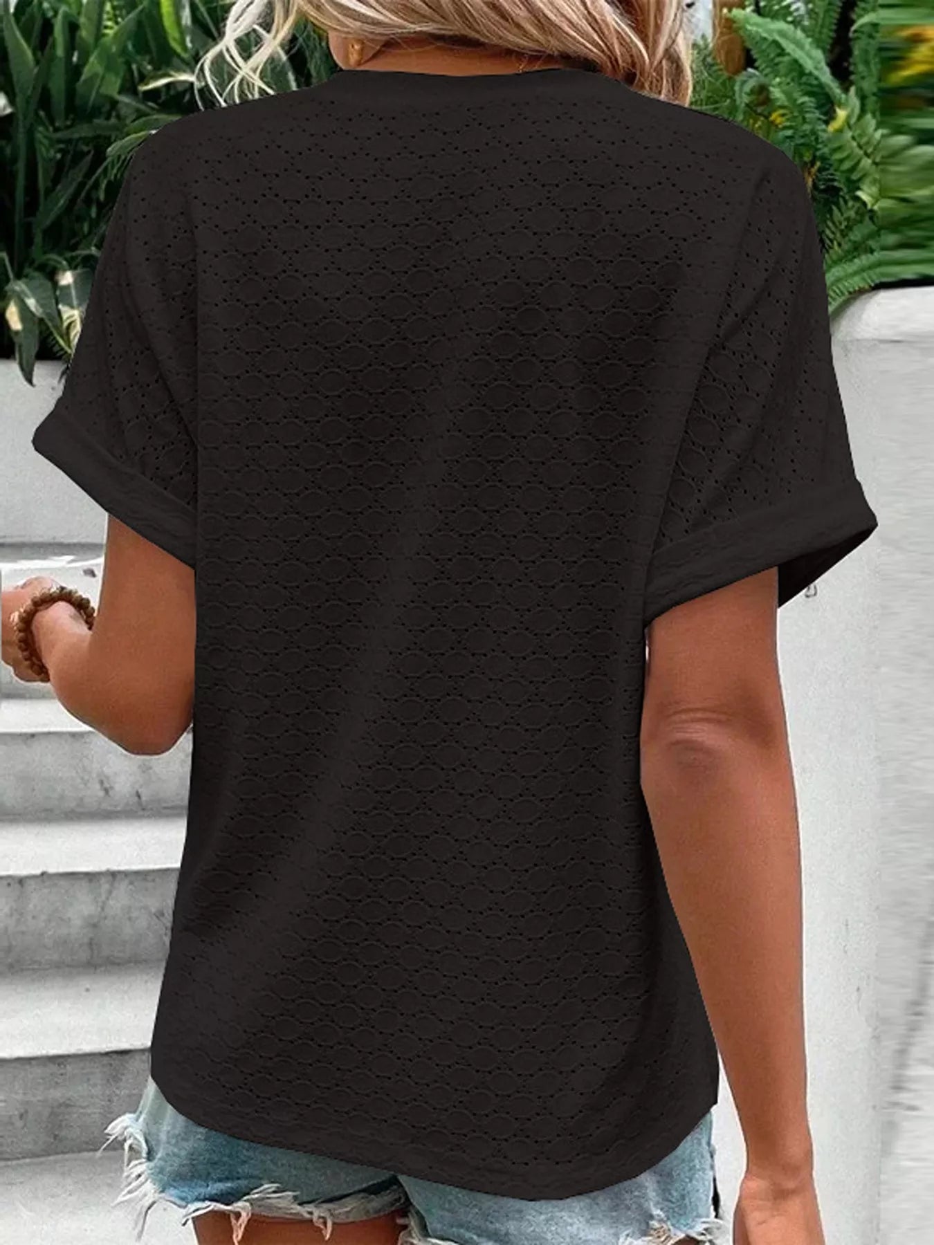 Back view of a black short-sleeve top featuring subtle textured eyelet pattern and cuffed sleeves