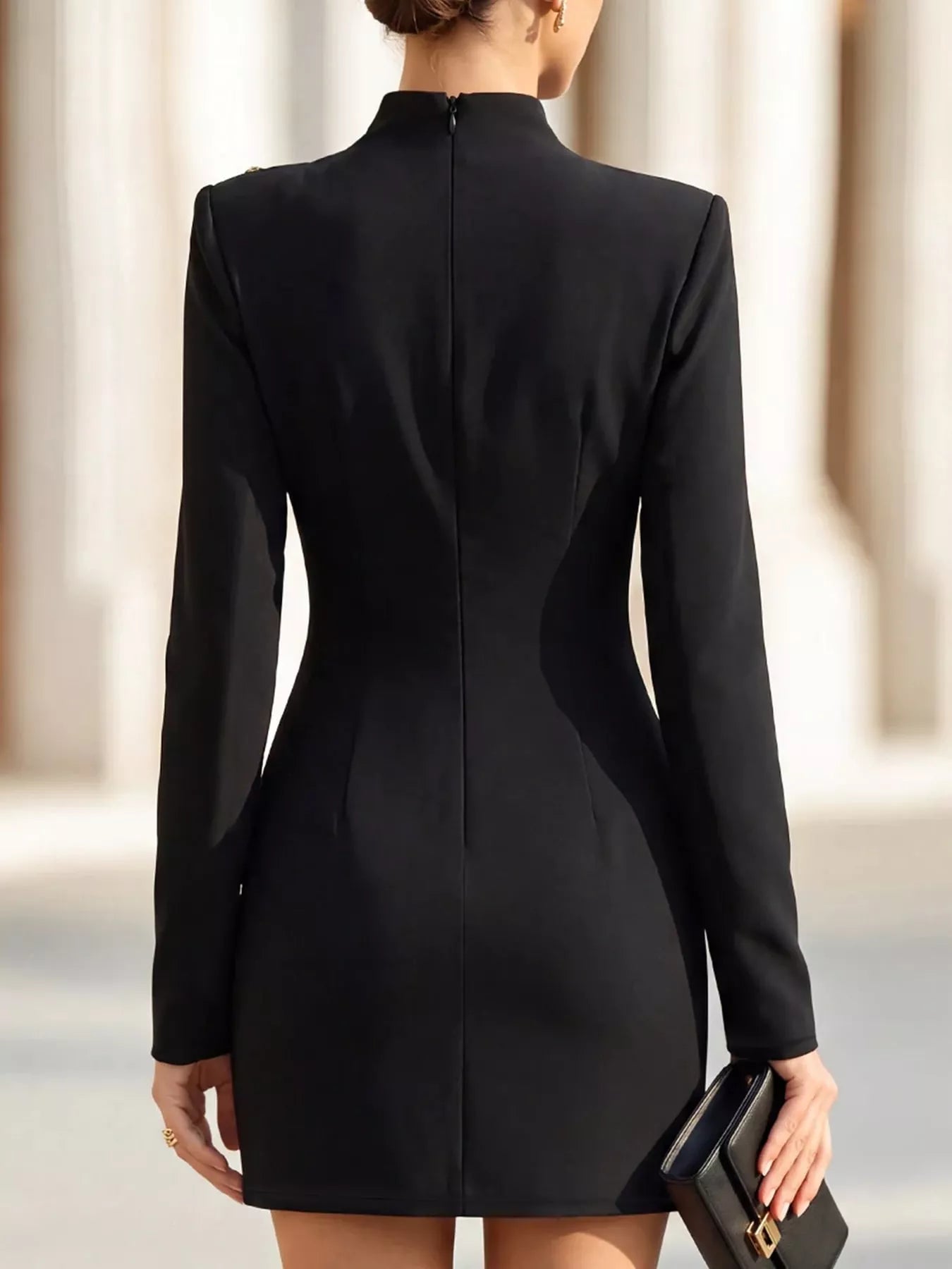 Back view of model outdoors wearing black mock neck mini dress with long sleeves and back zip