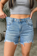 Women's asymmetric denim shorts with distressed whiskering and raw hems.