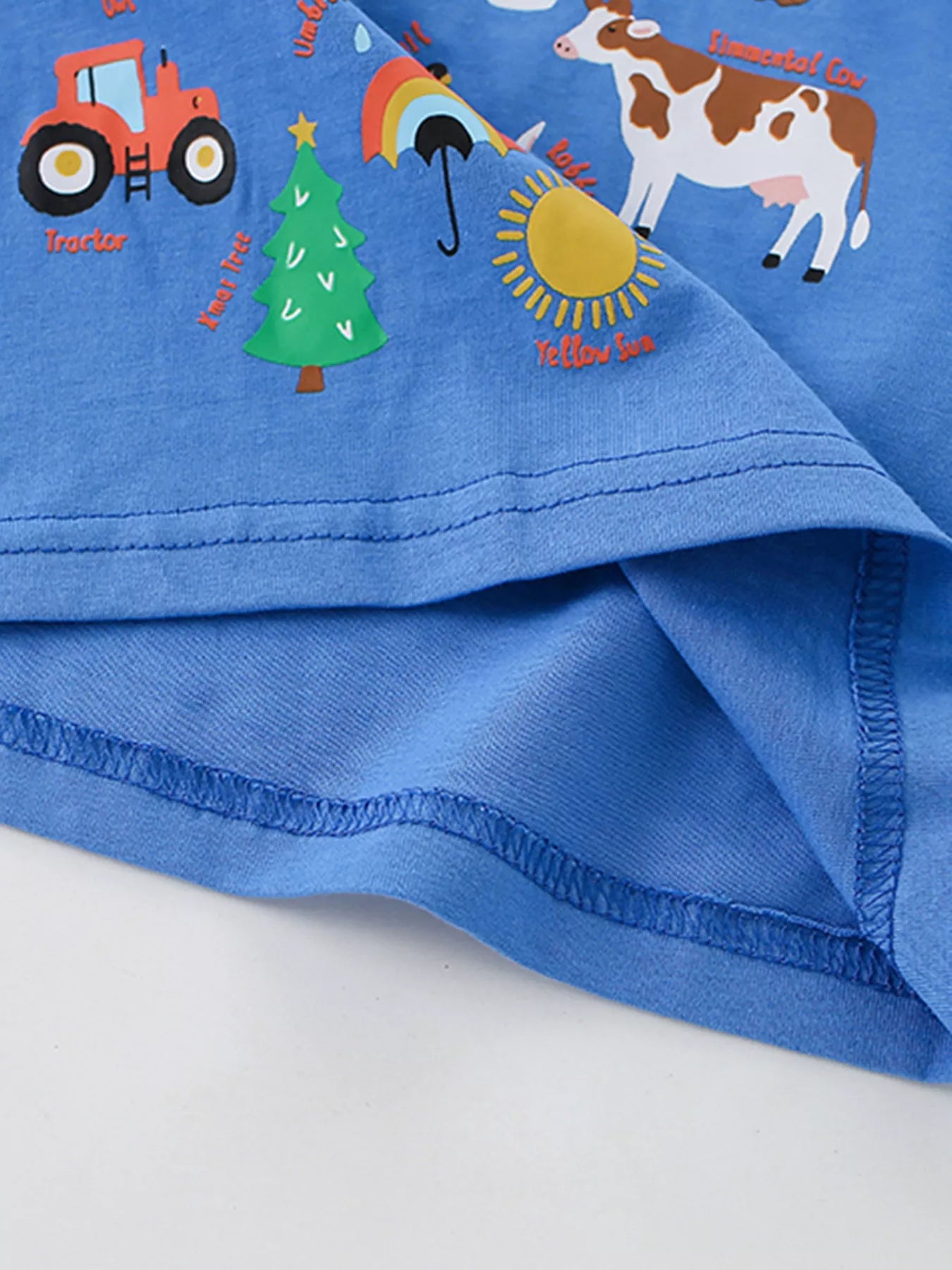 Close-up of lower farm alphabet print with tractor tree sun and cow beside blue hem stitching