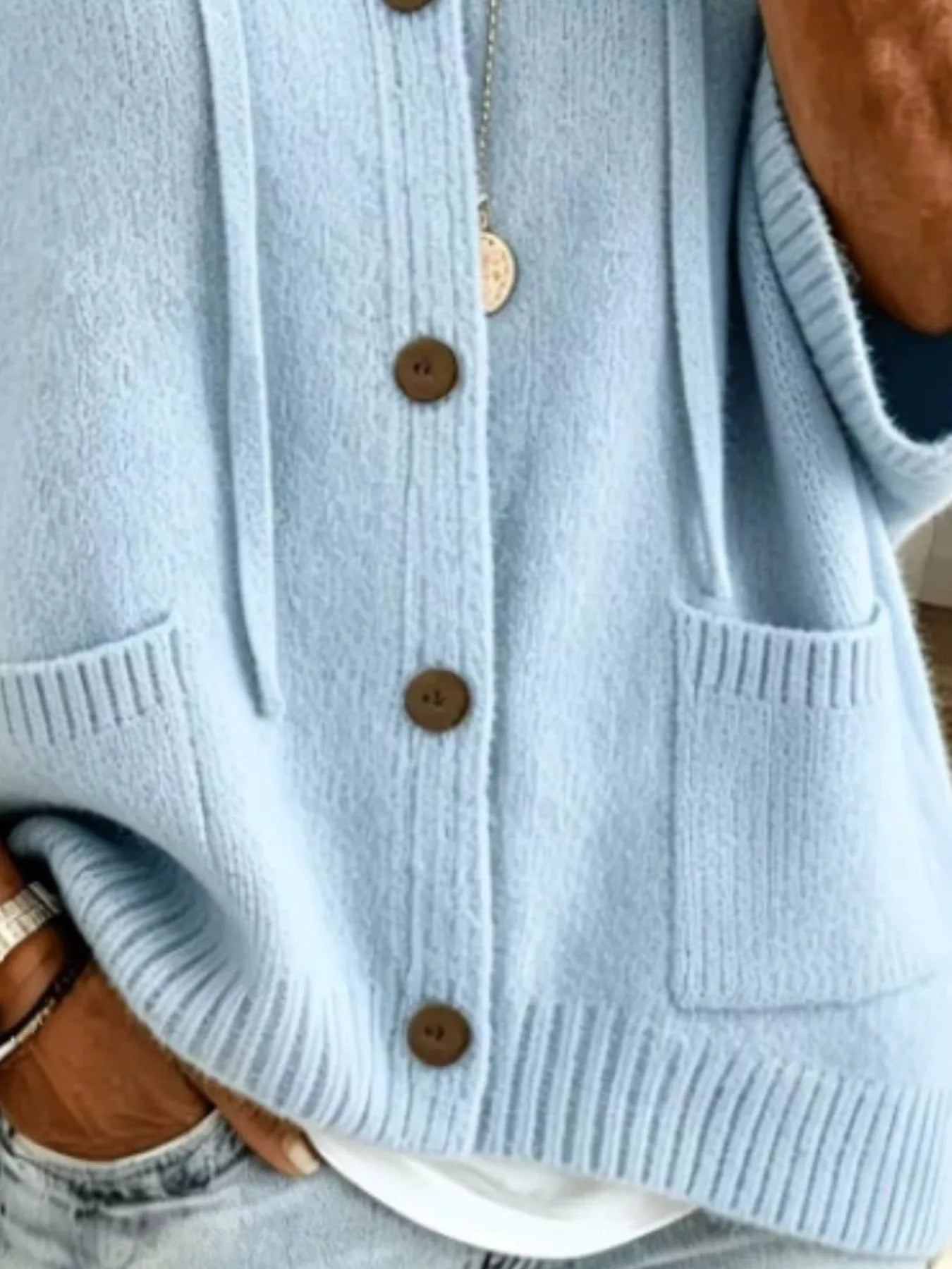 Detail view of the sky blue cardigan showing brown buttons, patch pockets and ribbed hem