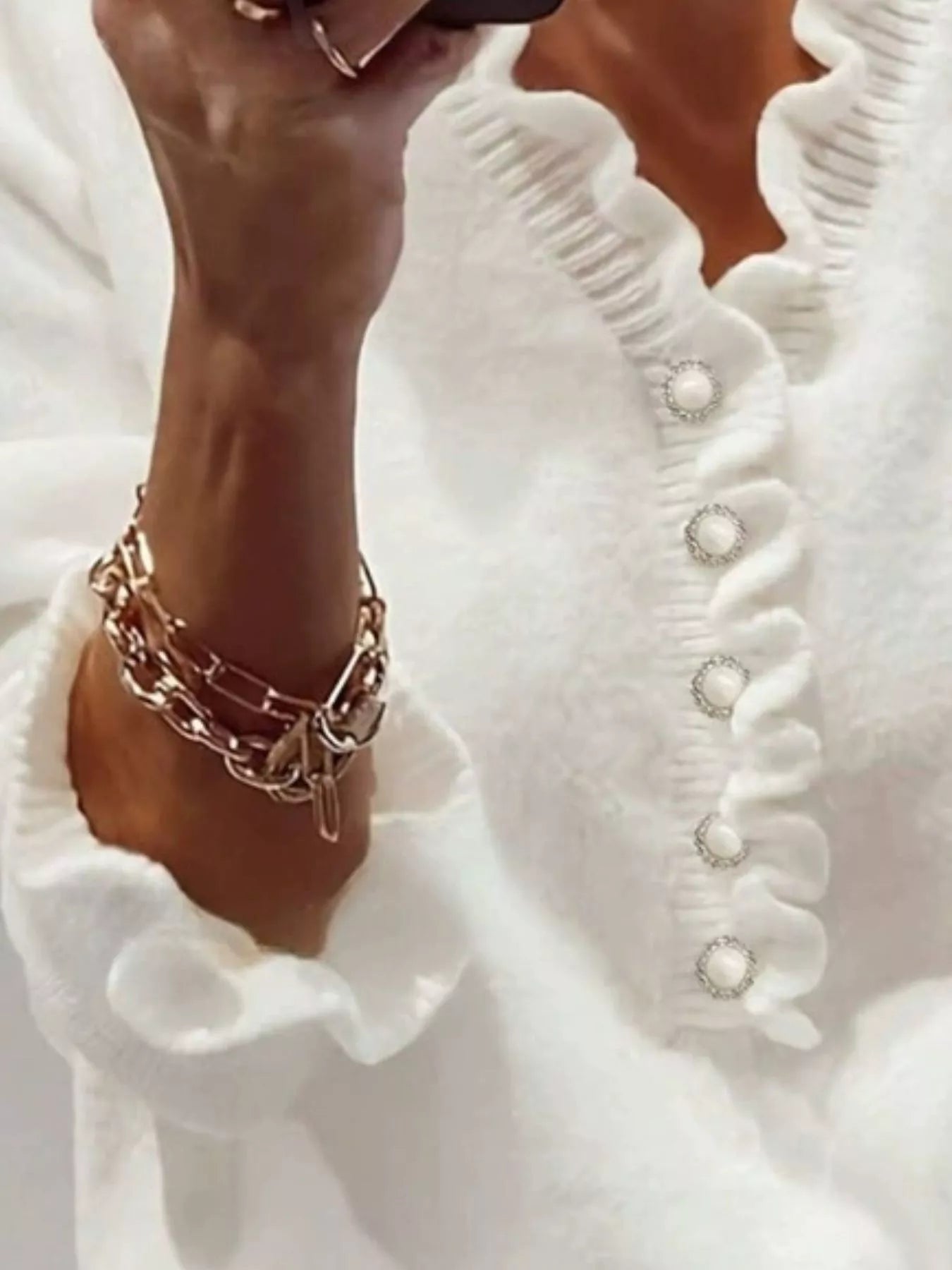 Close front view of a white ruffled sweater with pearl buttons