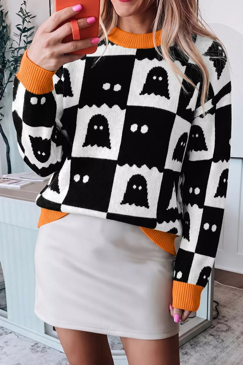 Mirror front view of a black and white ghost checkerboard sweater with orange cuffs