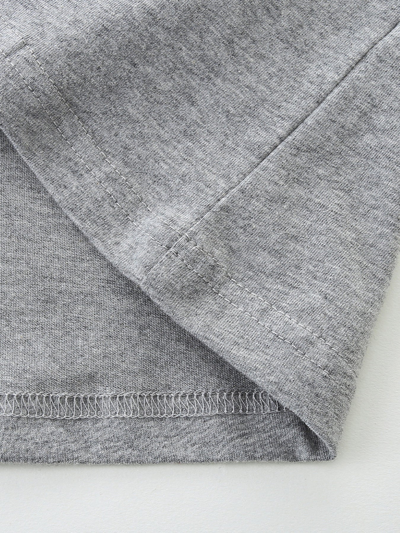 Close up of gray children's t-shirt hem and sleeve stitching with heathered fabric texture