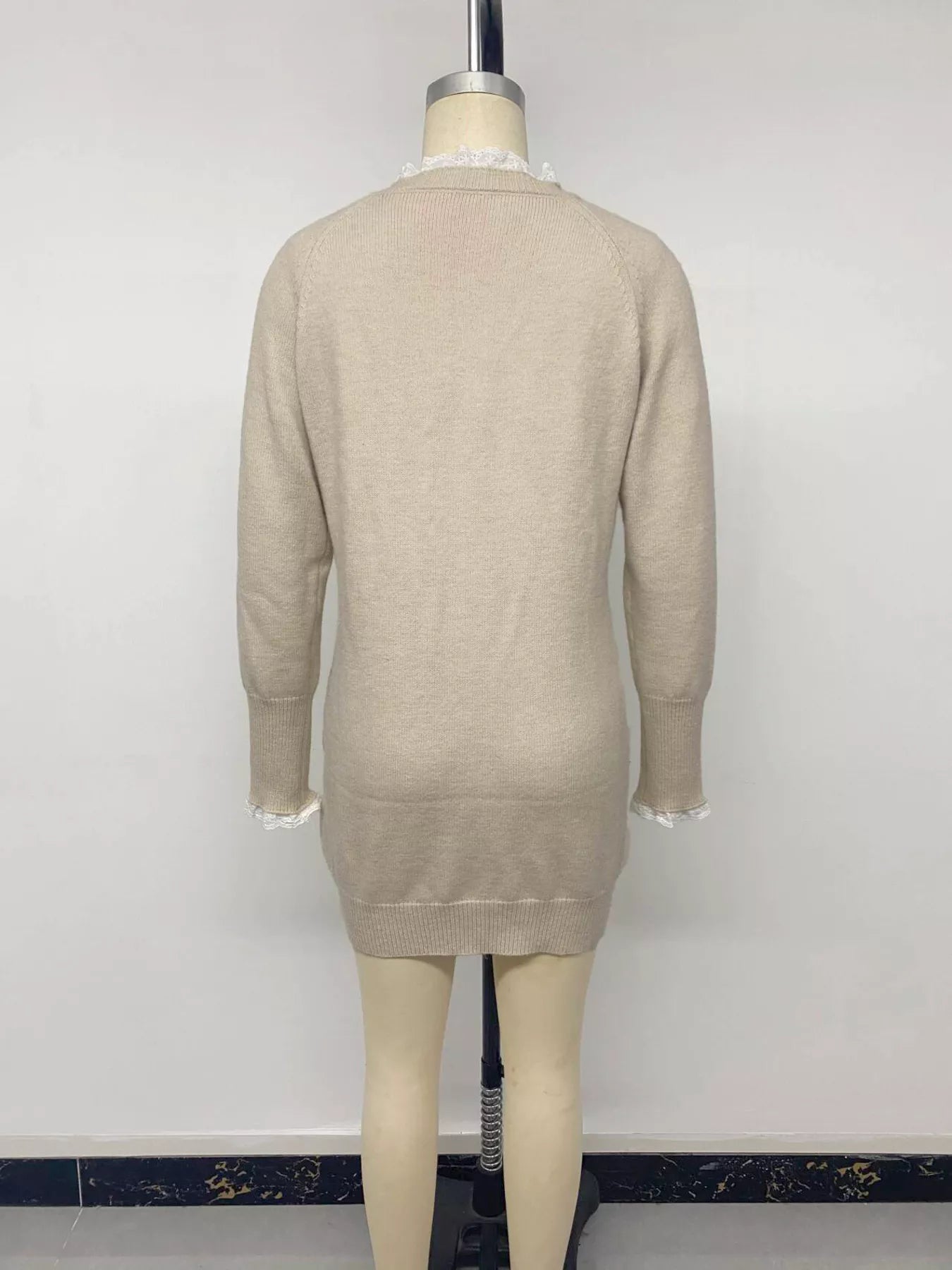 Back view of beige cable knit sweater dress on a mannequin with lace trim and raglan sleeves