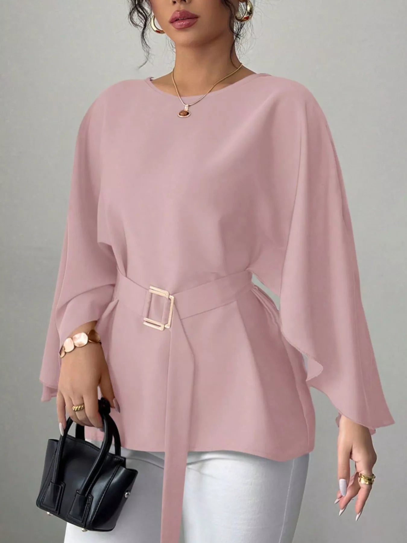 Pink round neck blouse front view holding black handbag with gold buckle belt