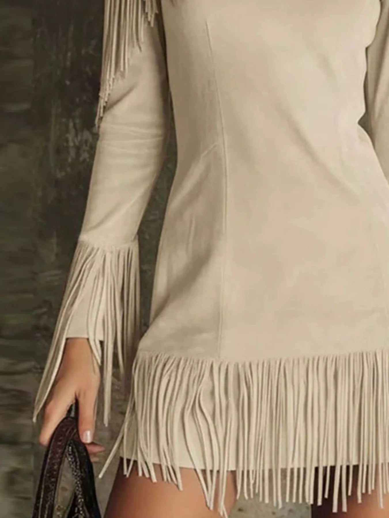 Close detail of the apricot fringed cold shoulder mini dress hem and sleeve fringe