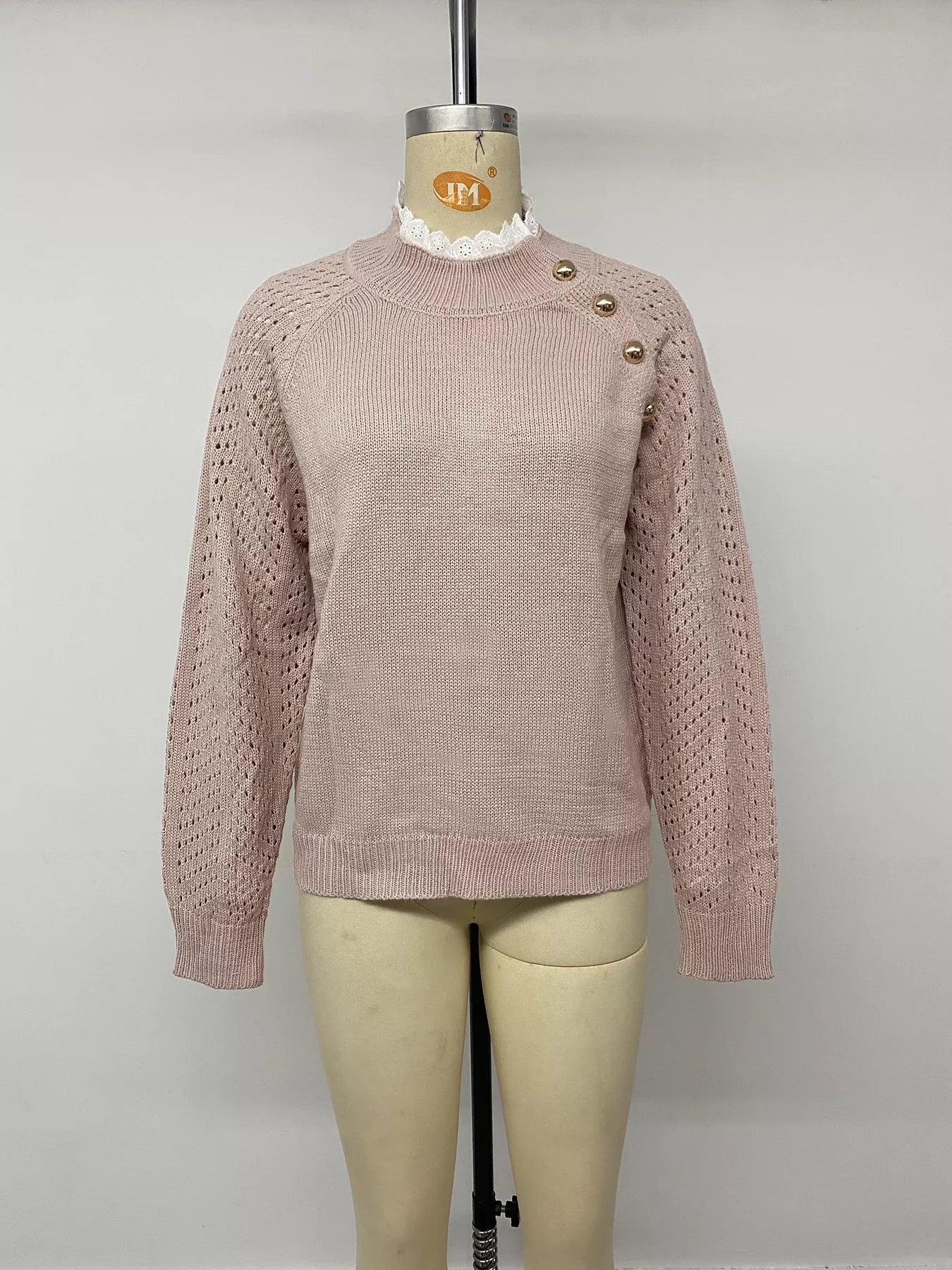 Front view on a mannequin of a pink openwork sweater with gold shoulder buttons