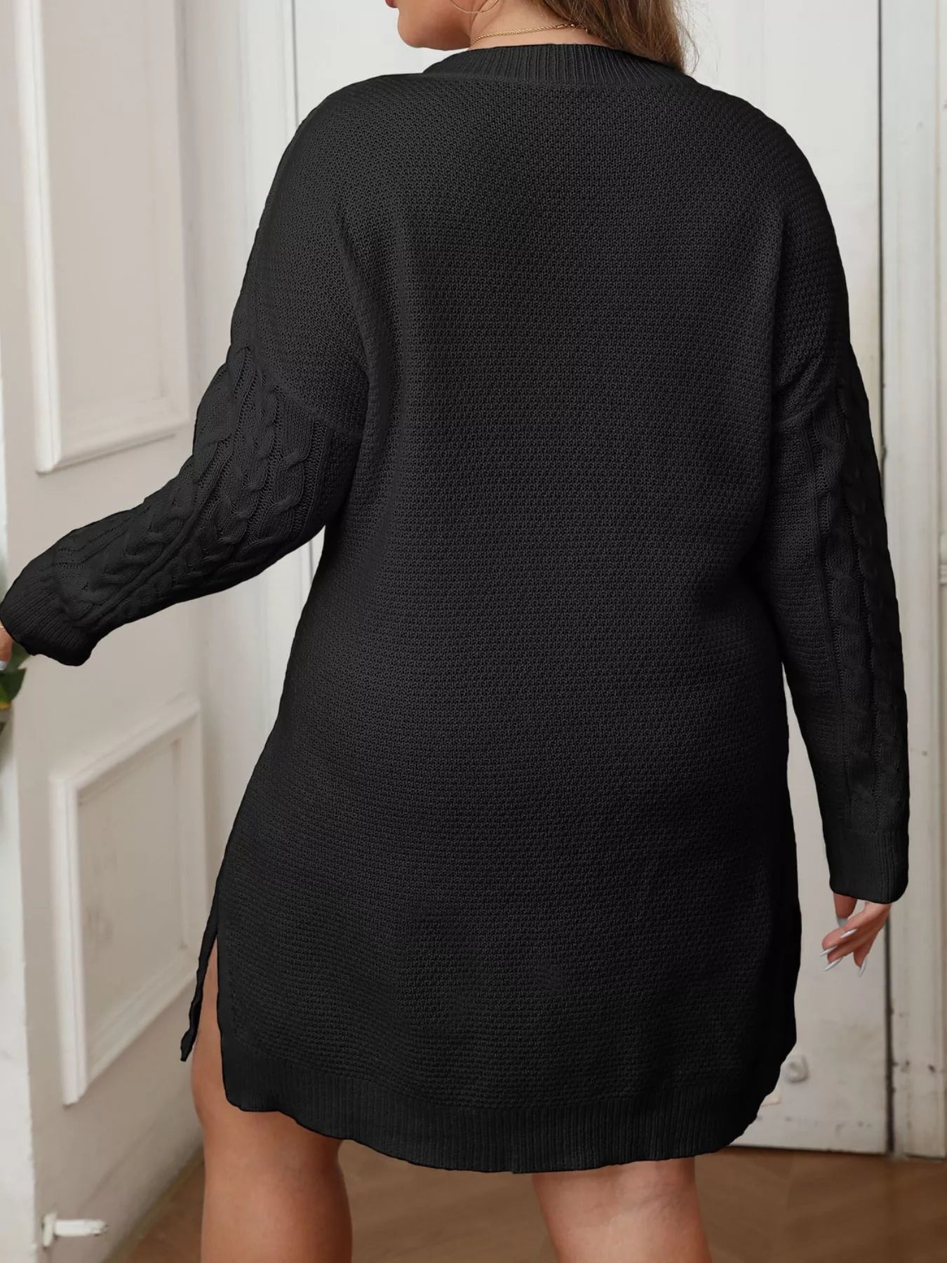 Back view of black cable knit sweater dress with long sleeves and side slit