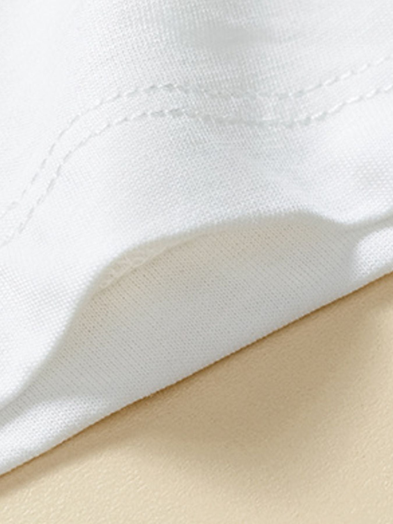 Detail view of white fabric and double stitching on the sleeve of a children's white short sleeve tee