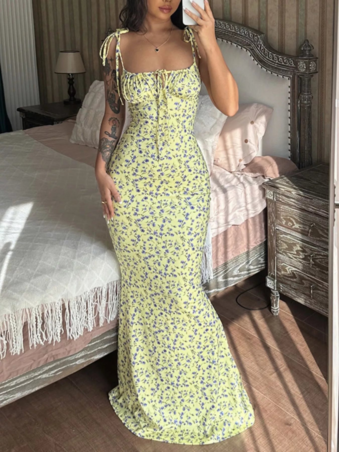 Model taking mirror selfie in yellow floral print bodycon maxi dress with tie straps and flared hem