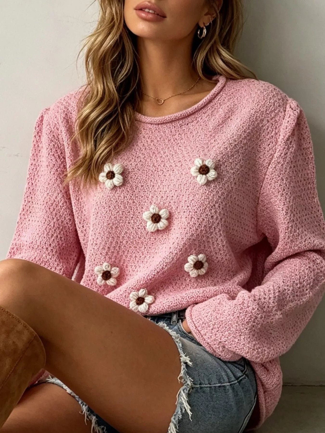 Close seated view of a pink textured knit sweater with white floral appliques