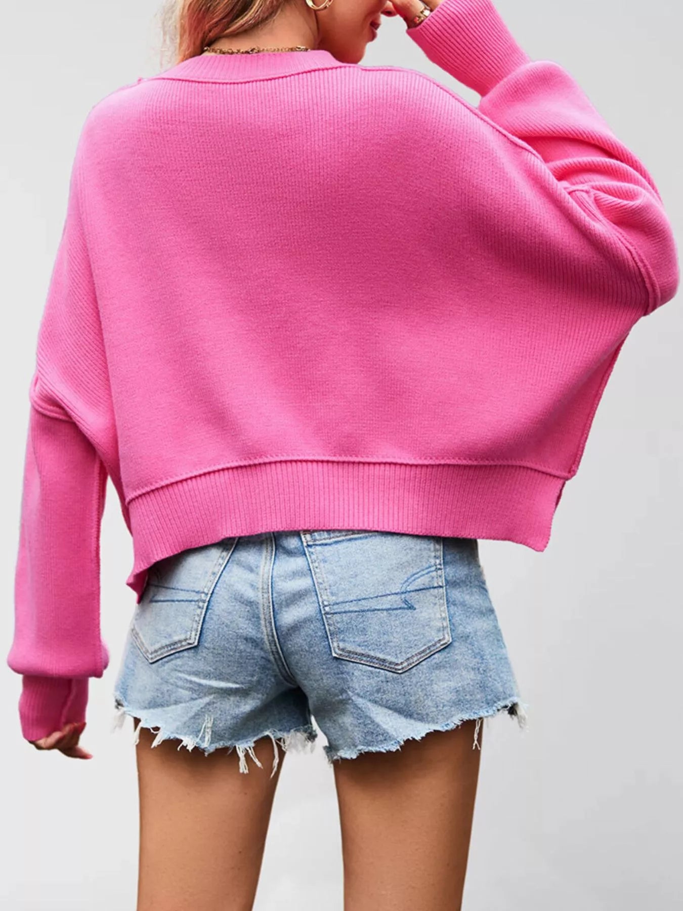 Back view of the bright pink crew neck dropped shoulder sweater with ribbed hem and long sleeves.