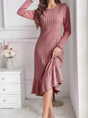 Dusty pink ribbed knit bodycon dress with ruffle hem worn indoors, front view lifting the skirt