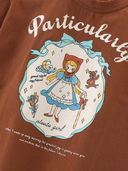 Close-up of cartoon girl graphic with blue bow frame on dark brown children's tee