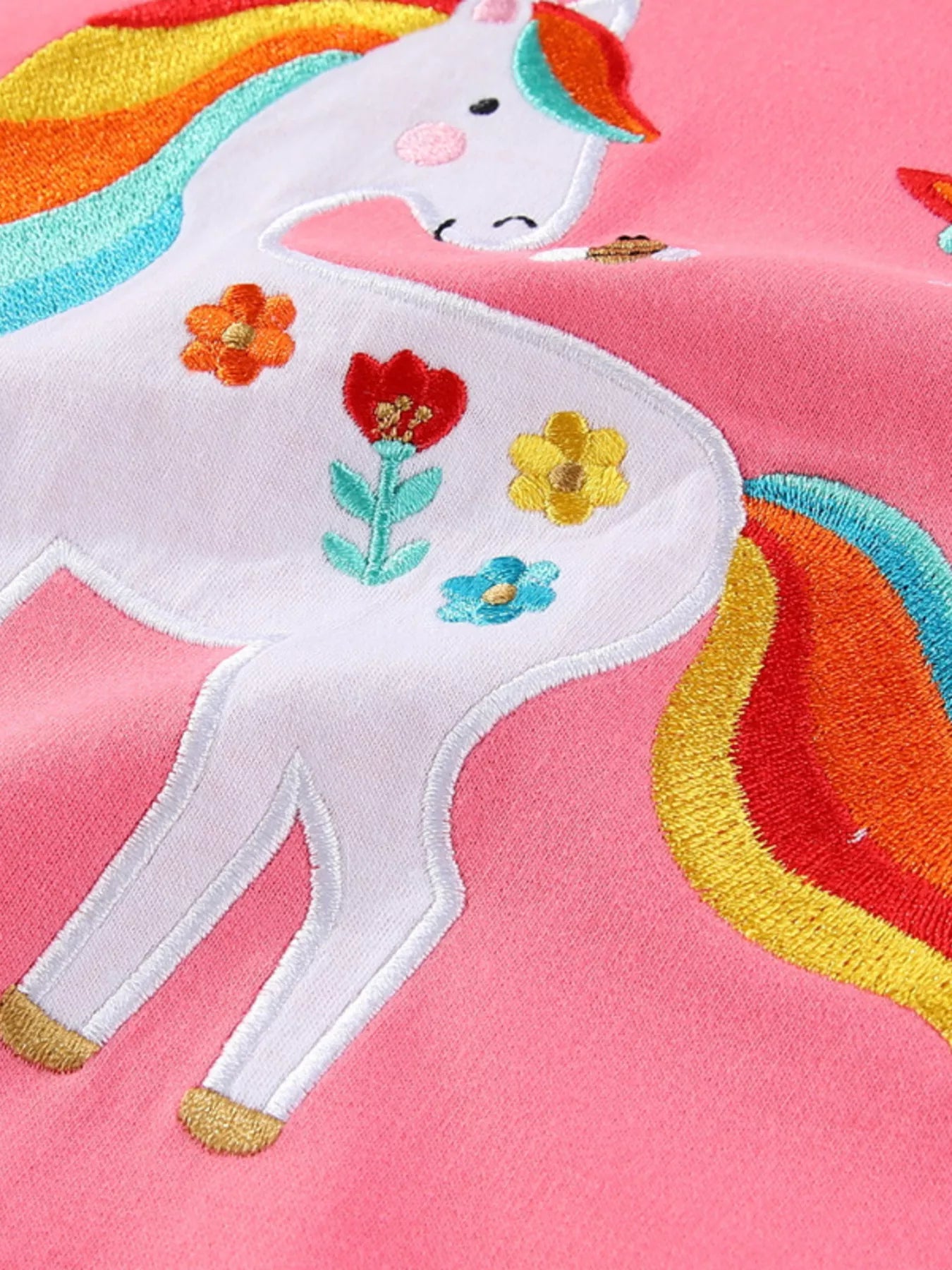 Close view of the embroidered white unicorn body with colorful flowers on pink fabric