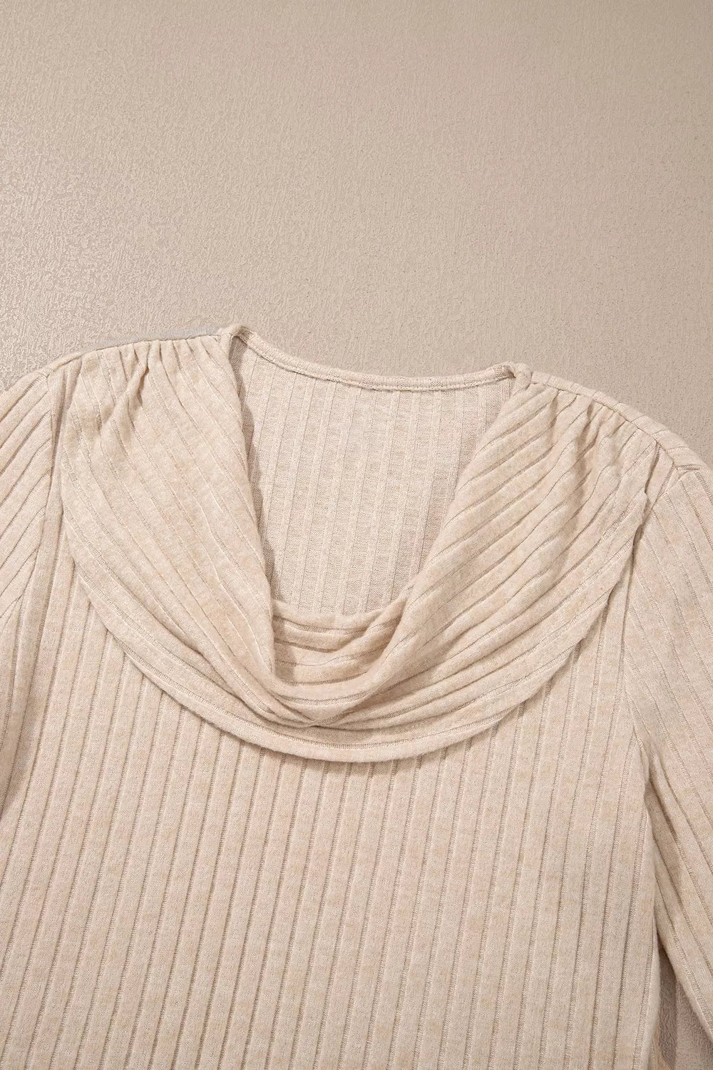 Close-up detail of a beige ribbed long-sleeve top featuring a draped cowl neckline