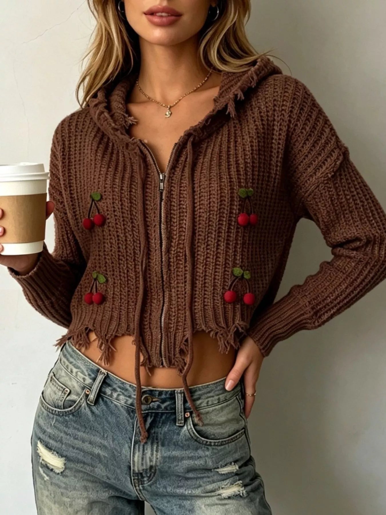 Brown knit zip up hooded sweater with red cherry appliques worn on model holding coffee