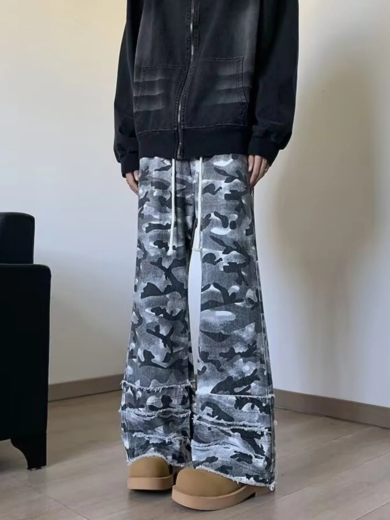 Men's grey camouflage wide leg jeans with white drawstrings and frayed raw hems, front view on model.