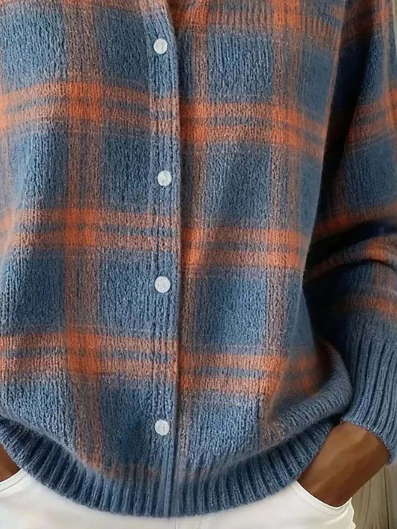 Close-up of the lower front and ribbed hem of a blue and orange plaid knit cardigan