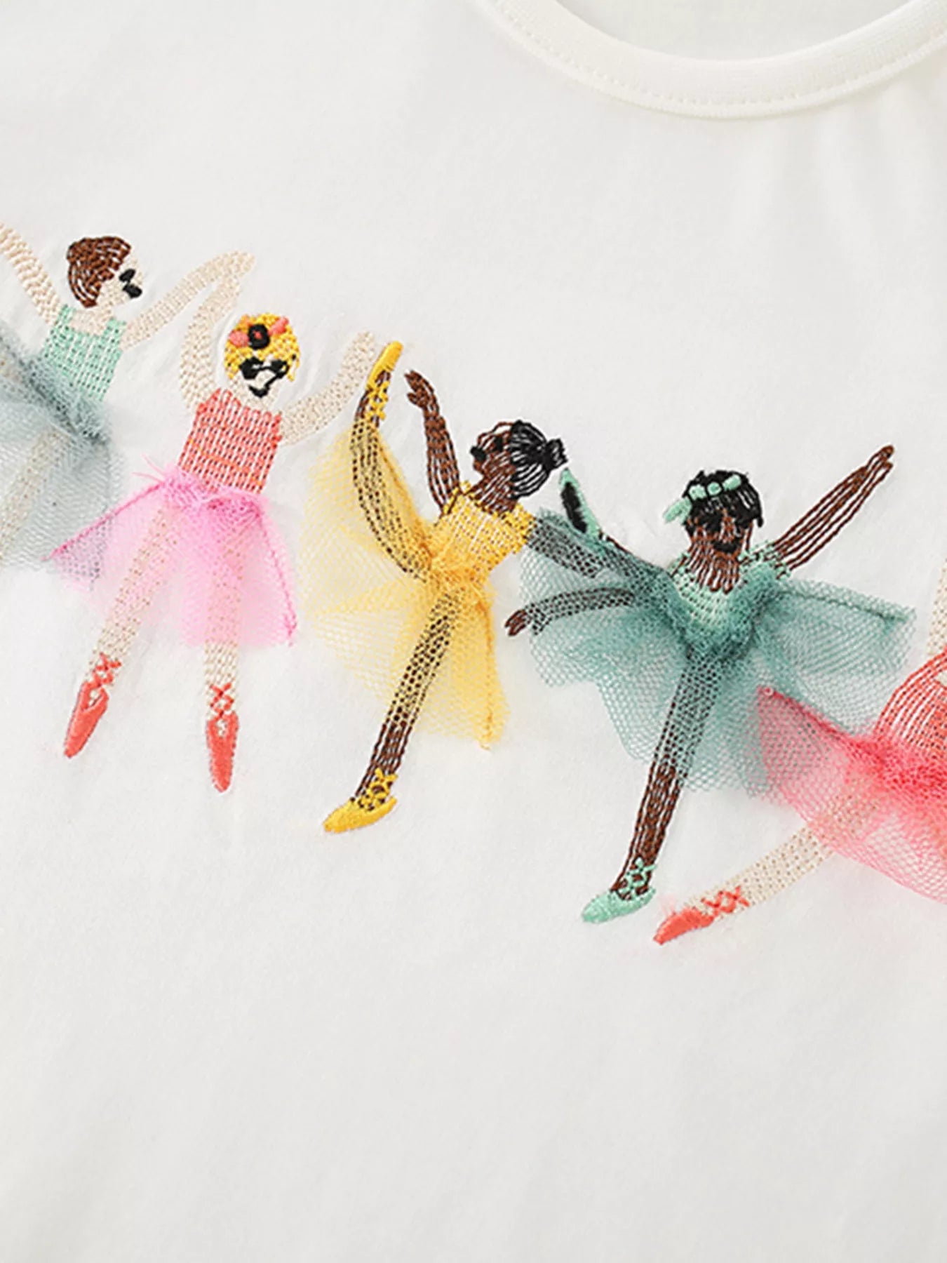 Detail view of embroidered ballet dancers in pink yellow and green tulle skirts on a white children's tee