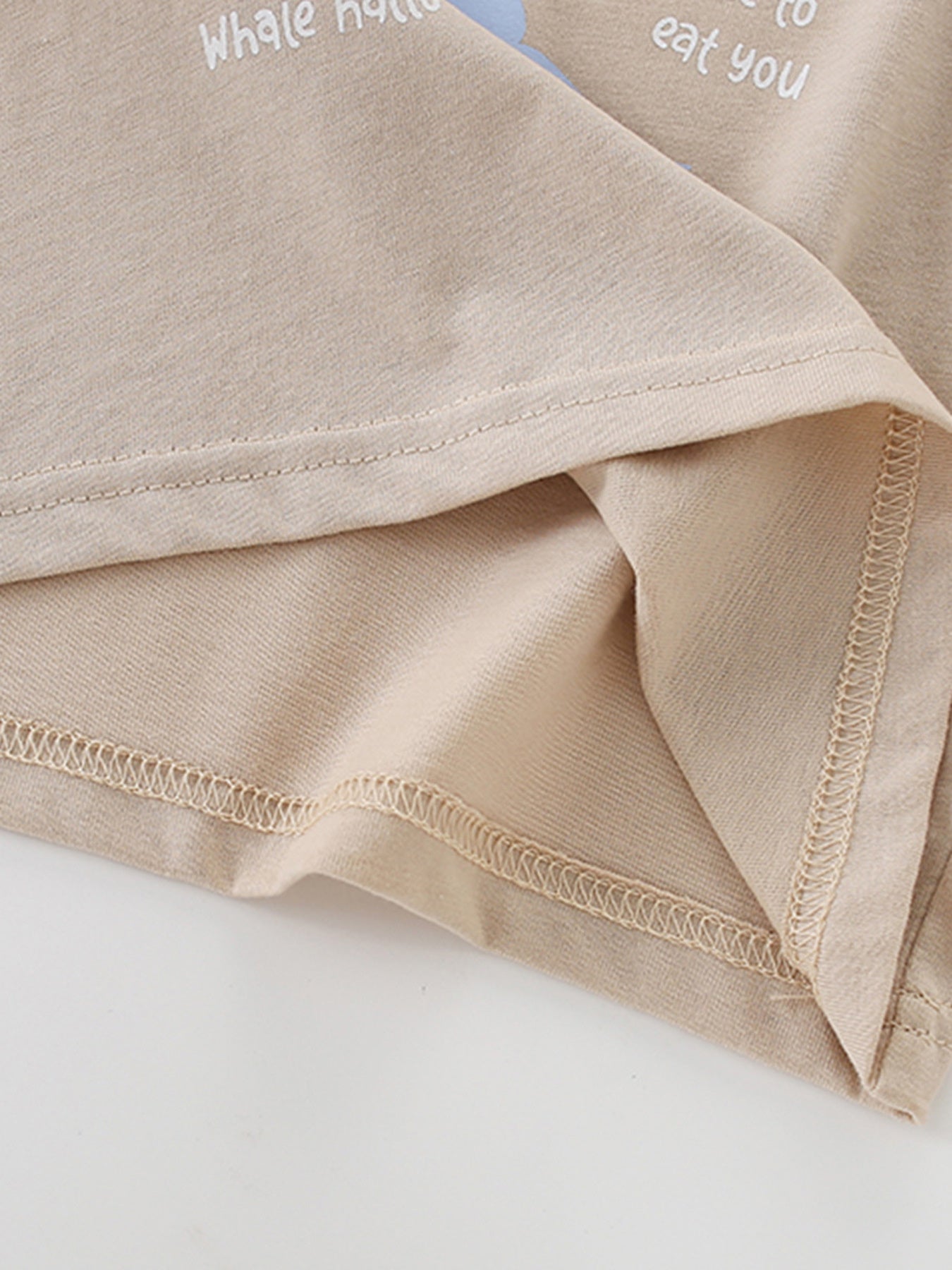 Close-up of the hem stitching and inner fabric on a tan children's ocean graphic short sleeve tee