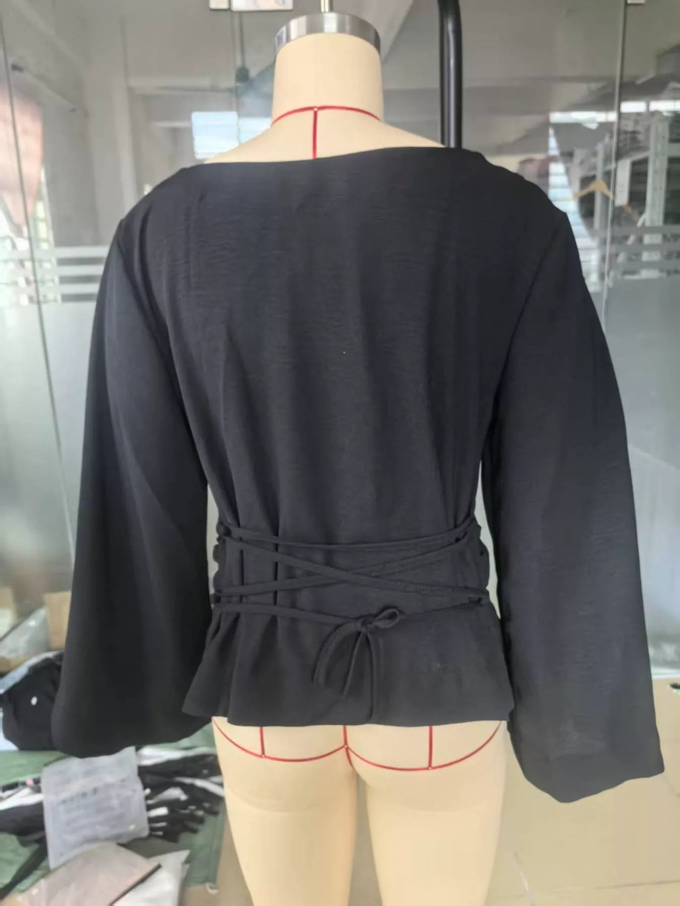 Back view of black boat neck long sleeve top with waist ties on mannequin indoors
