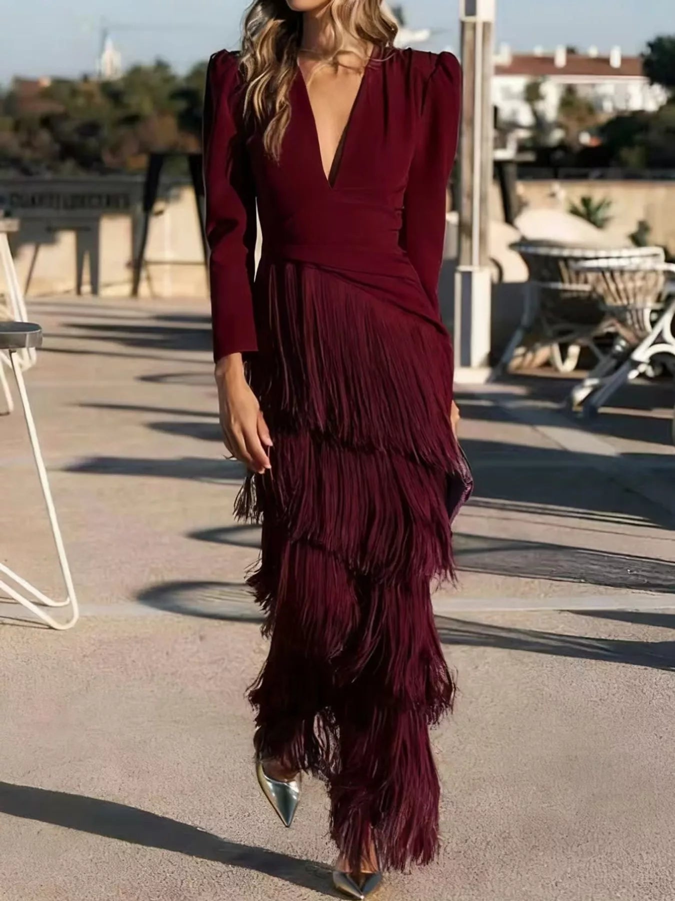 Full length view of a burgundy fringed maxi dress with puff sleeves worn walking outdoors