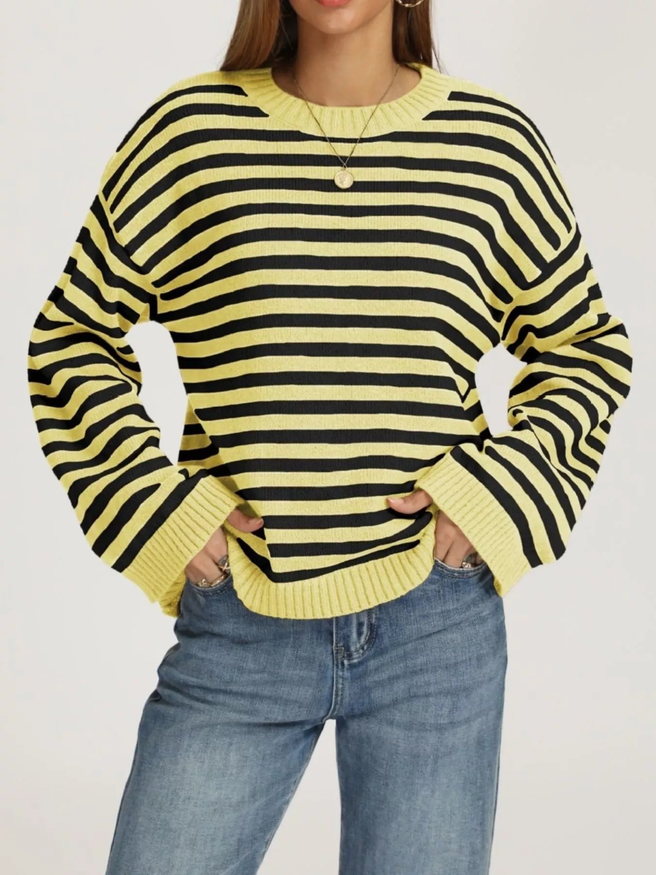 Front view of a yellow and black striped dropped shoulder sweater with ribbed cuffs worn with jeans.