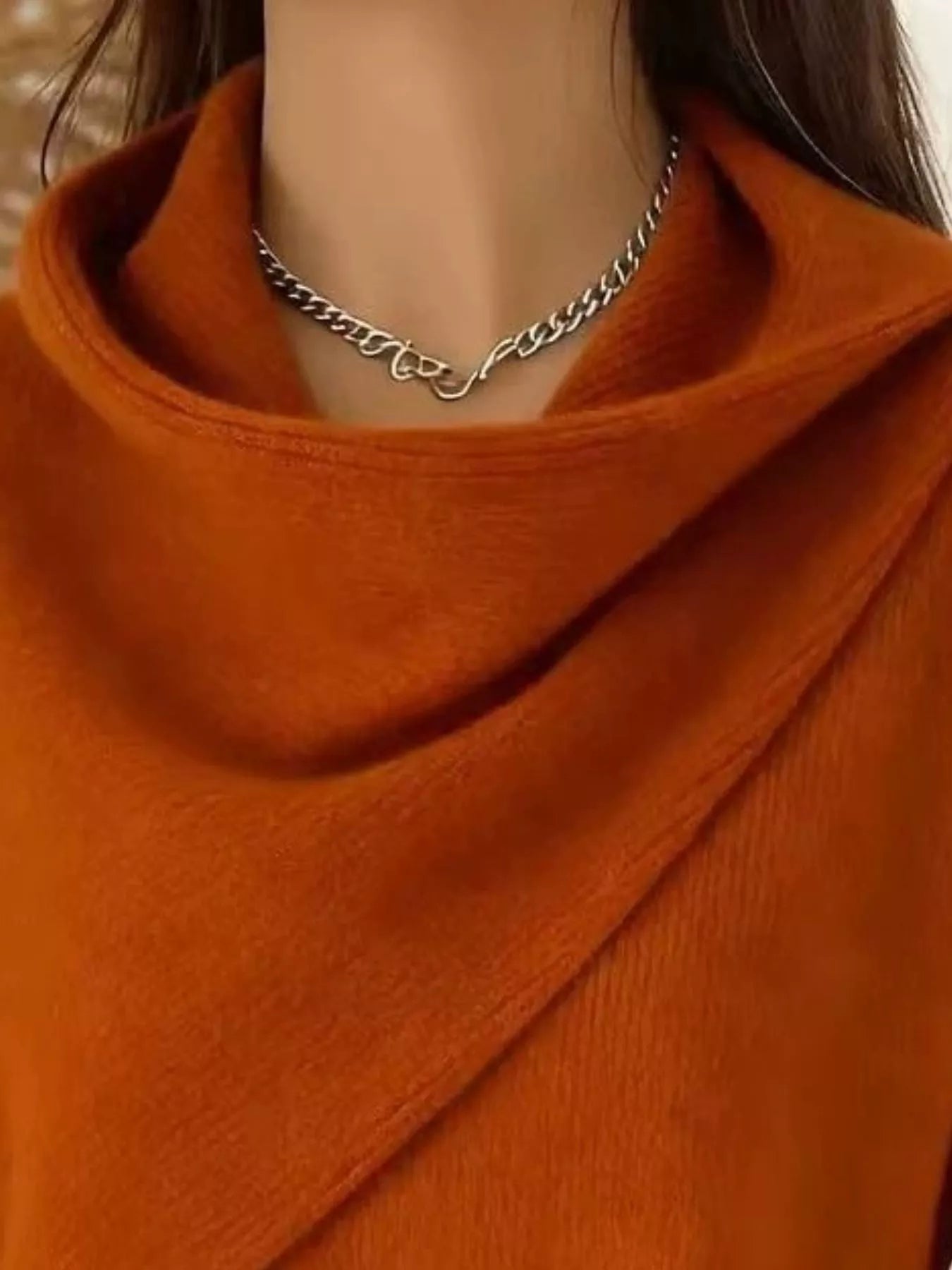 Close-up of the burnt orange cowl neckline showing the draped asymmetric collar and fine knit texture