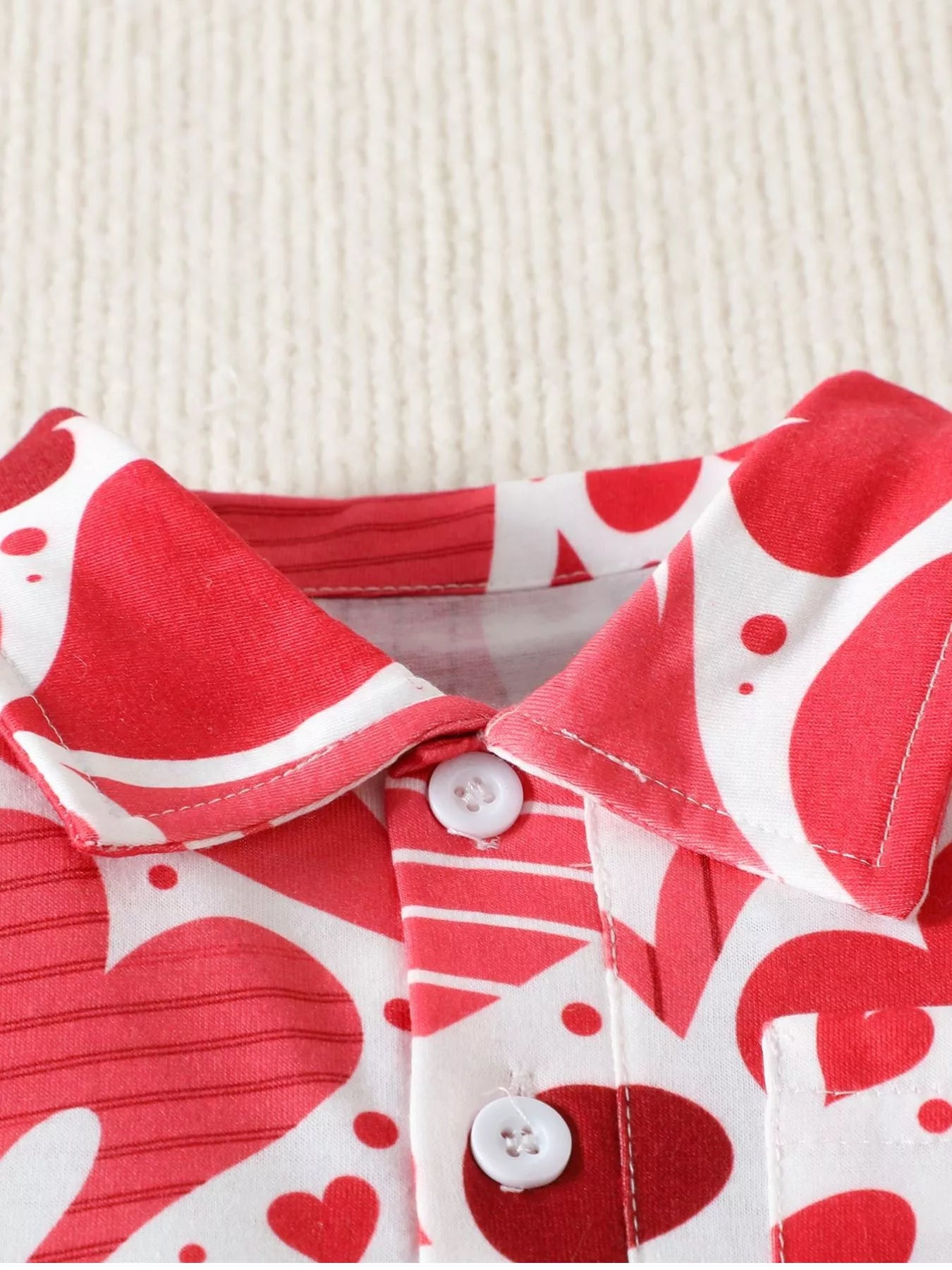 Close up of the polo collar and white buttons on a red and white children's heart print shirt