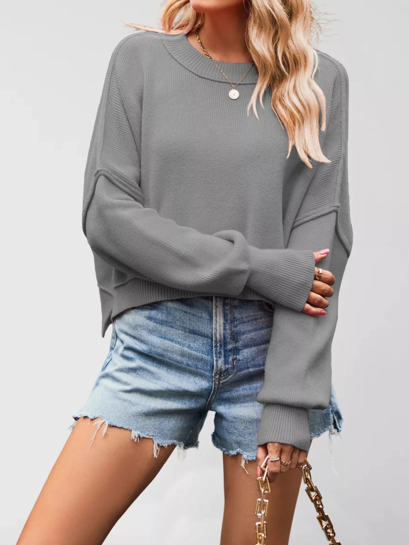 Front view of a gray crew neck dropped shoulder sweater with ribbed cuffs worn with denim shorts.