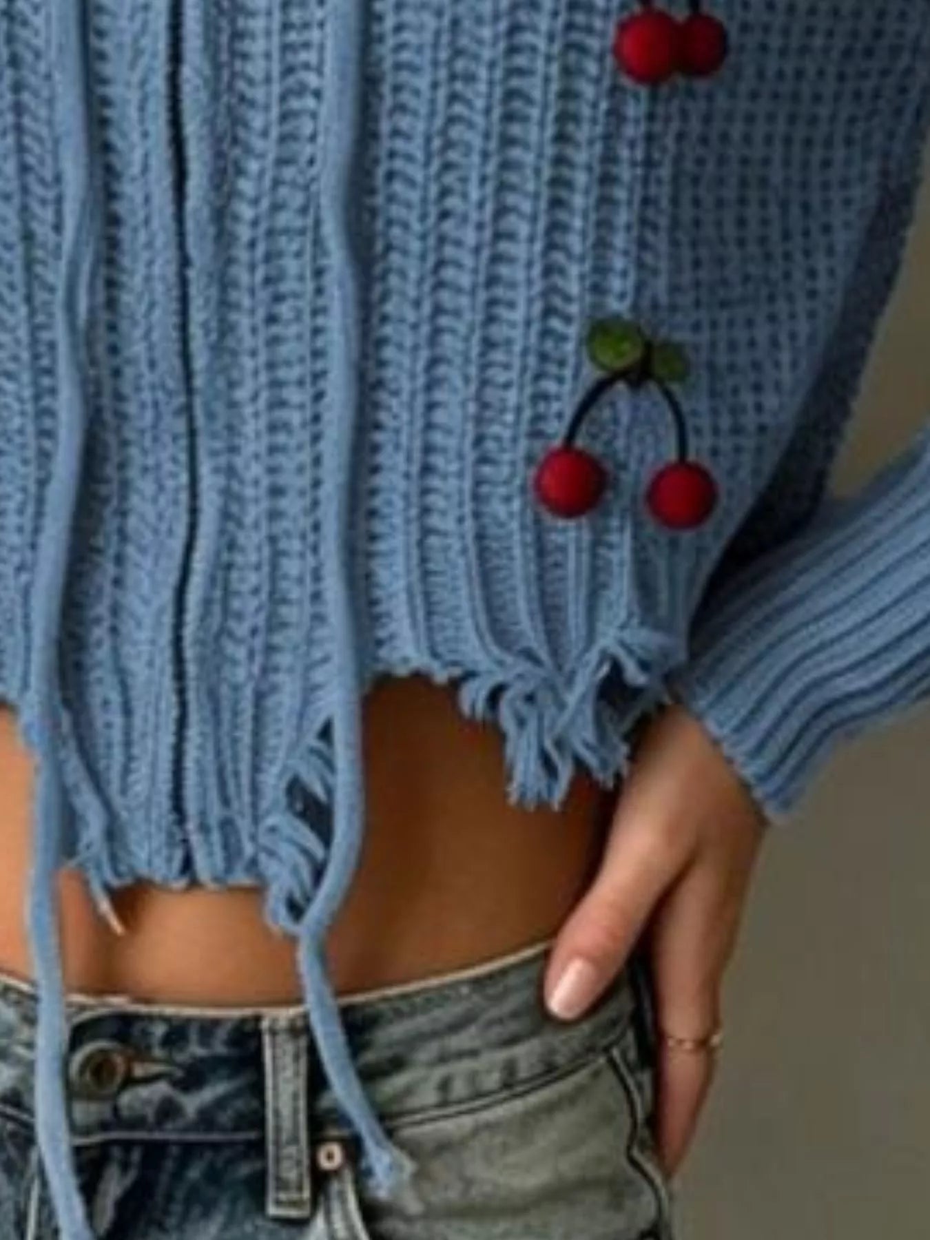 Close up of dark blue knit sweater showing frayed hem, drawstrings and red cherry applique