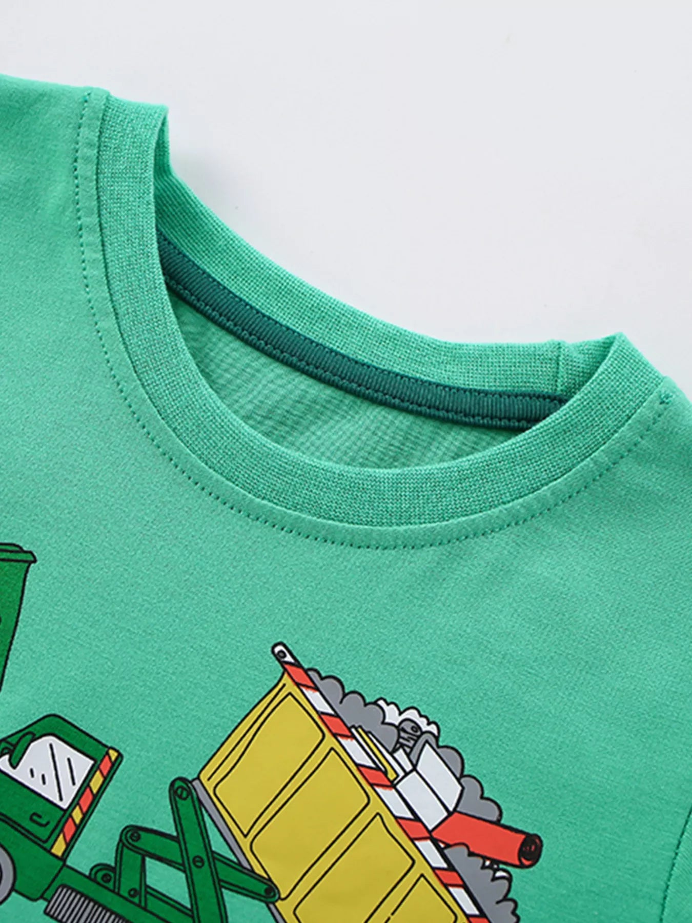Close-up of the ribbed round neckline on the green children's T-shirt, with part of the cartoon truck print below