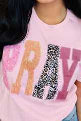 Close-up of pink graphic tee featuring sequined leopard-print patches spelling “PRAY” on the front