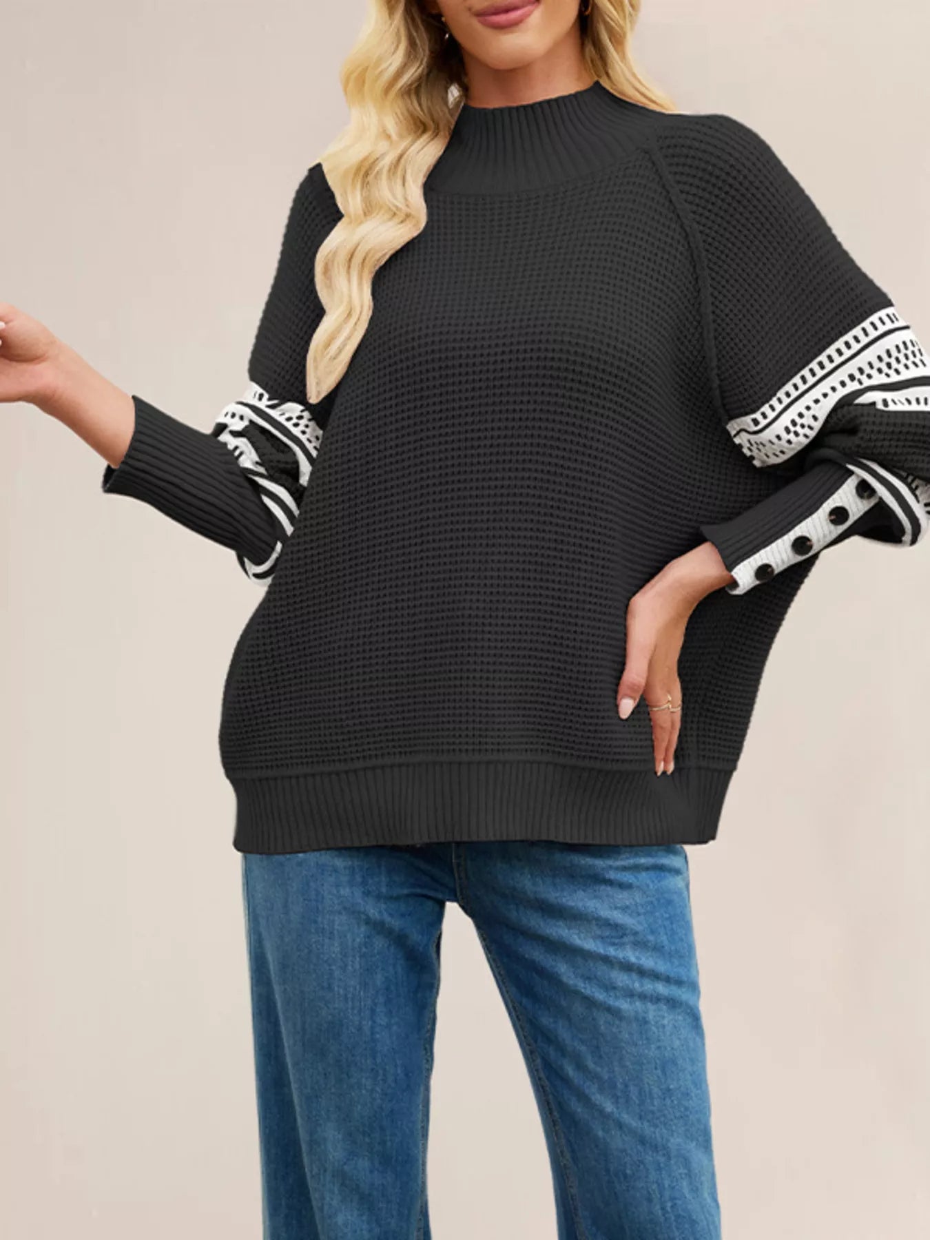Front view of the black waffle knit sweater with white patterned sleeves, hand on hip.