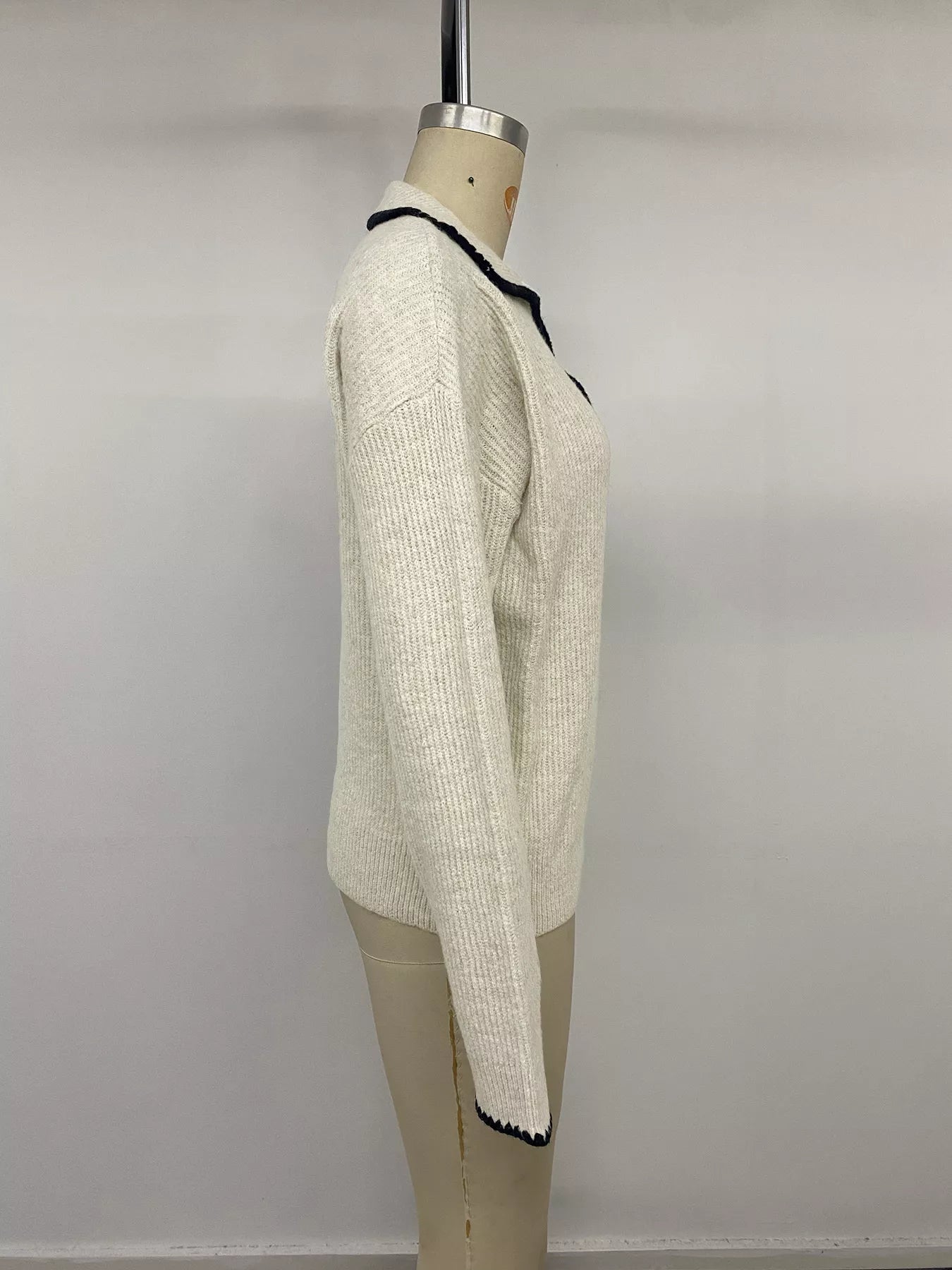 Side view on a mannequin of a cream sweater with black scalloped collar and cuff trim