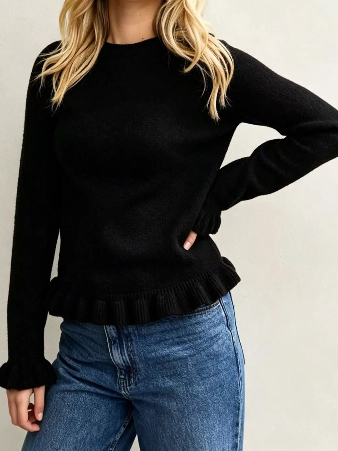 On-model front view of black crew neck sweater with ruffled hem and cuffs