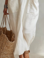 Cropped lower view of white sleeveless scoop neck maxi dress, showing pockets and flowing skirt