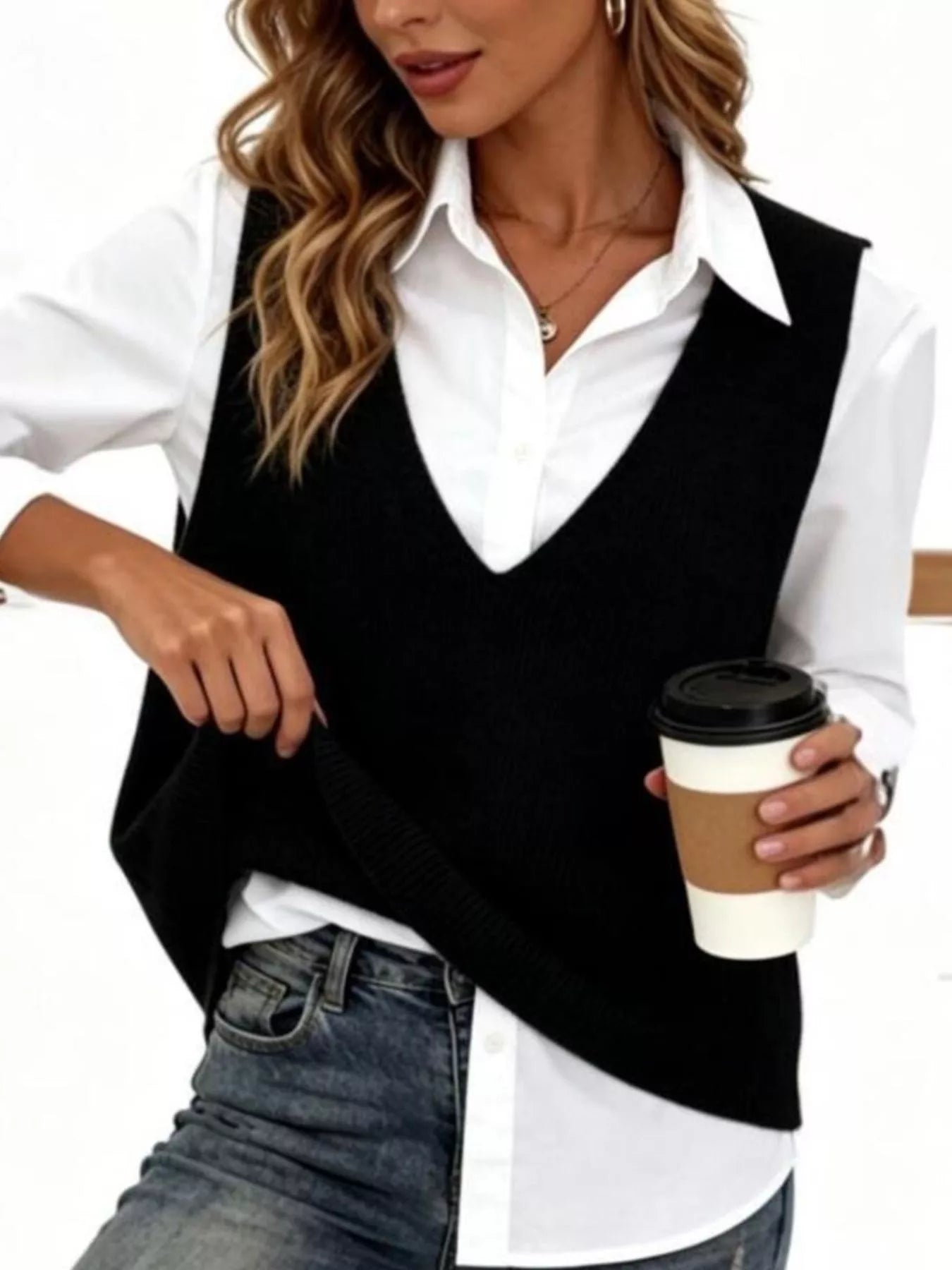 Black V neck knit sweater vest over white shirt, model holding coffee and lifting hem