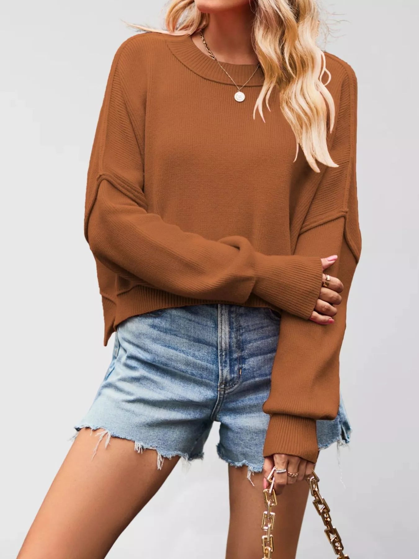 Front view of a camel crew neck dropped shoulder sweater with ribbed cuffs worn with denim shorts.
