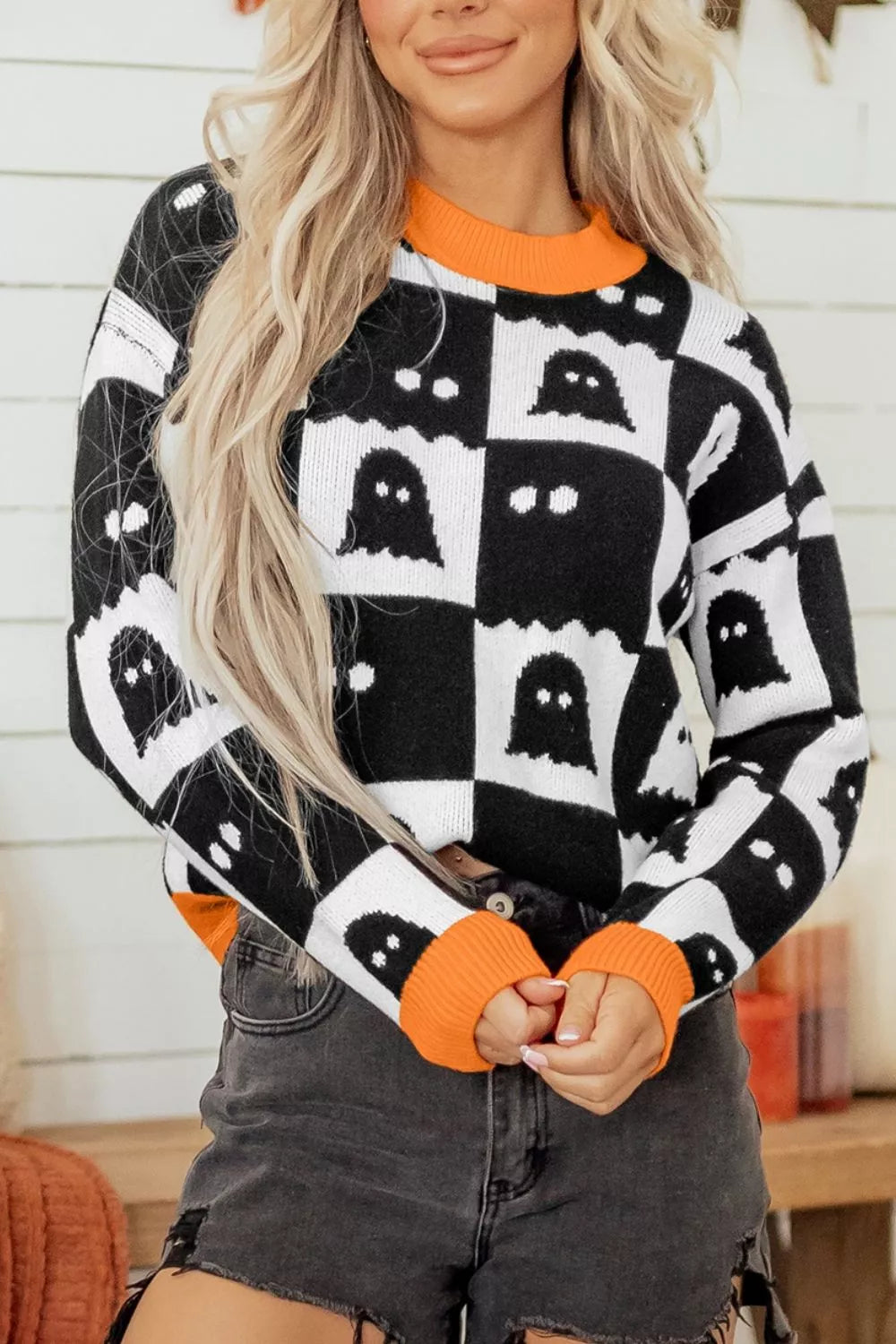 Front view of a checkerboard ghost sweater with orange round neck and ribbed cuffs